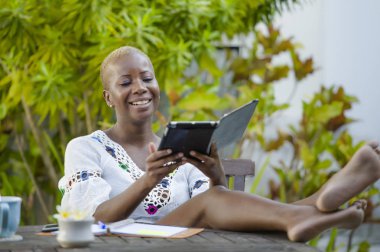 Dijital tablet ile açık havada rahat ve neşeli dijital göçebe başarılı seyahat ve yaşam tarzı blogger serbest iş kafede çalışan genç mutlu ve çekici siyah afro Amerikan kadın