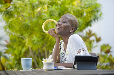 Genç güzel ve mutlu siyah Afrika kökenli Amerikalı hipster kadının açık havada kafede dijital tablet dijital göçebe başarılı yaşam tarzı kavramı kulaklık ile müzik dinlemek ile çalışma
