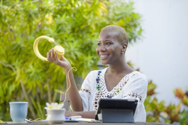 Genç güzel ve mutlu siyah Afrika kökenli Amerikalı hipster kadının açık havada kafede dijital tablet dijital göçebe başarılı yaşam tarzı kavramı kulaklık ile müzik dinlemek ile çalışma