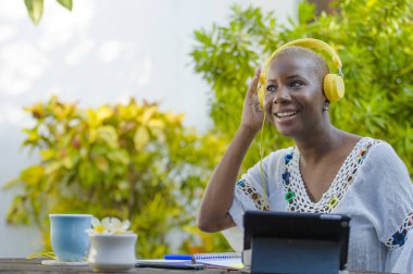Genç güzel ve mutlu siyah Afrika kökenli Amerikalı hipster kadının açık havada kafede dijital tablet dijital göçebe başarılı yaşam tarzı kavramı kulaklık ile müzik dinlemek ile çalışma