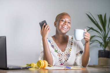 evde cep telefonu dijital göçebe ve serbest meslek işi başarı gülümseyen Internet kullanarak dizüstü bilgisayar ile office çalışan genç mutlu ve çekici siyah afro Amerikan hipster kadın