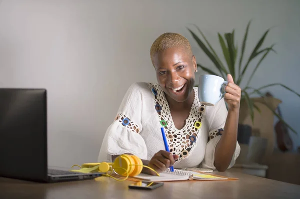 young happy and attractive hipster black afro American woman drinking tea or coffee at home office working cheerful with laptop computer in digital nomad self-employed and internet job concept