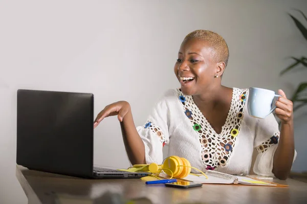 young happy and attractive hipster black afro American woman drinking tea or coffee at home office working cheerful with laptop computer in digital nomad self-employed and internet job concept