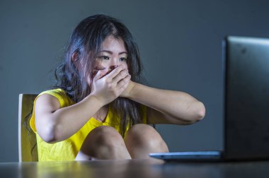 dramatic portrait of scared and stressed Asian Korean teenager girl or young woman with laptop computer suffering cyber bullying stalked and harassed with internet social media password hacked clipart