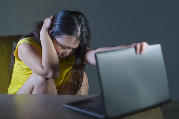 dramatic portrait of scared and stressed Asian Korean teenager girl or young woman with laptop computer suffering cyber bullying stalked and harassed with internet social media password hacked