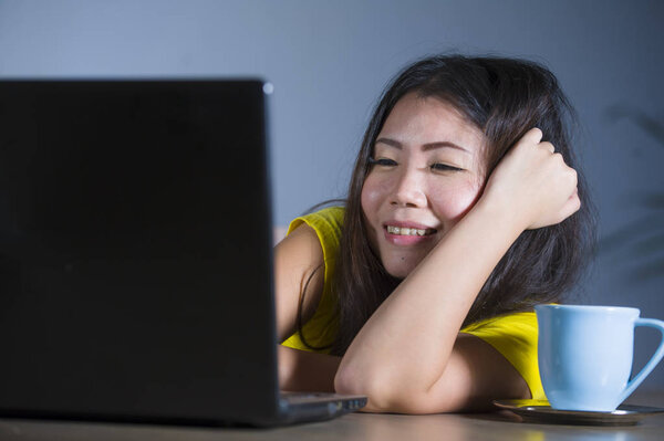 young pretty and happy Asian Korean woman at desk enjoying internet on laptop computer smiling cheerful having fun drinking tea cup at home isolated on grey background in lifestyle concept