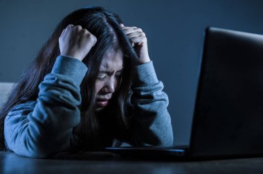 young worried Asian Korean student girl looking depressed and desperate studying with laptop computer in stress for exam feeling frustrated stalked and harassed on internet bullying clipart