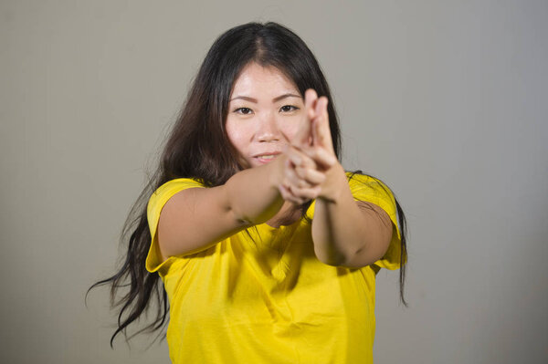 young playful and happy woman or teenager in yellow t-shirt gesturing with hands as if pointing a gun having fun isolated on grey background in gestures and expressions concept