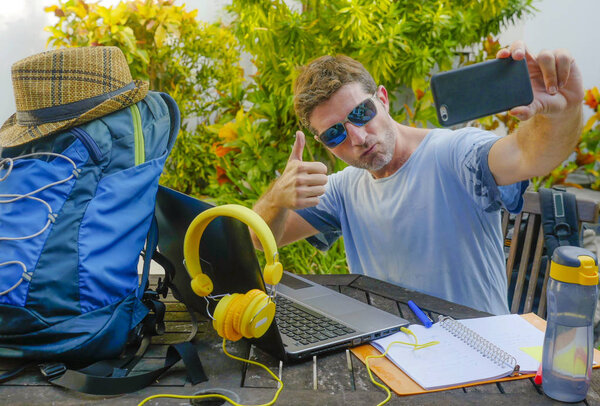 young attractive and happy digital nomad man working outdoors with laptop computer cheerful taking selfie pic with mobile phone in freelancer and independent job success concept