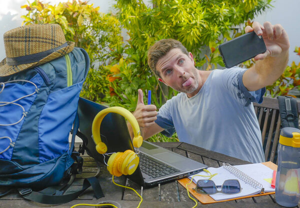 young attractive and happy digital nomad man working outdoors with laptop computer cheerful taking selfie pic with mobile phone in freelancer and independent job success concept
