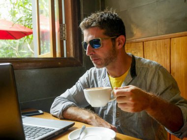 girişimci ve modern dijital göçebe iş kavramı internet kafede dizüstü bilgisayar ve cep telefonu ile çalışan genç çekici mutlu ve başarılı bin yıllık adam rahat