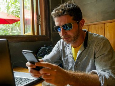 girişimci ve modern dijital göçebe iş kavramı internet kafede dizüstü bilgisayar ve cep telefonu ile çalışan genç çekici mutlu ve başarılı bin yıllık adam rahat