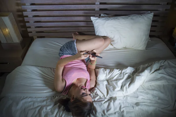 美しく 幸せな少女笑顔と彼女のデートでラインでベッドルームと携帯電話技術に明るくリラックスした携帯電話を使用してインターネットのソーシャル メディア アプリにいちゃつくのベッドで横になっています — ストック写真