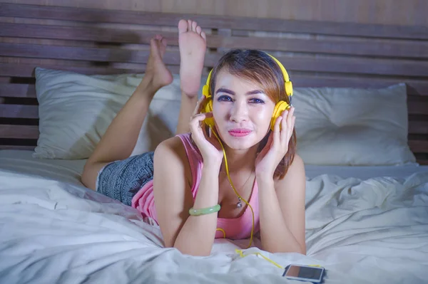 Genç çekici ve mutlu kız yatakta sarı kulaklıklarla rahat ve neşeli şarkı ve dans telefon ile internet üzerinden müzik dinlemek — Stok fotoğraf