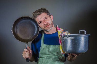 genç çekici vurguladı ve bunalmış tembel adam tutarak mutfak önlük ile pan ve stres tencereye ve iç çalışma ve dağınık ev kocası izole sinirli arka plan yemek 