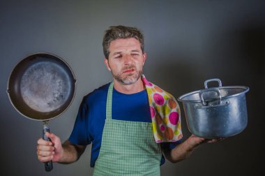 genç çekici vurguladı ve bunalmış tembel adam tutarak mutfak önlük ile pan ve stres tencereye ve iç çalışma ve dağınık ev kocası izole sinirli arka plan yemek 