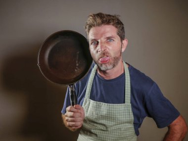 genç çekici vurguladı ve iç çalışma ve dağınık ev kocası arka plan mutfak tavada stres ve hayal kırıklığına uğramış surat ifadesi tutan önlük ile bunalmış tembel adam izole 