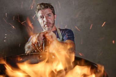 Genç komik ve dağınık ev mutfak felaket ve vasıfsız unexperienced korkunç ev aşçı gıda iç pişirme dağınıklığa yanan ateşi tavada tutan şok önlük adamla yemek