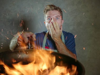 Genç komik ve dağınık ev mutfak felaket ve vasıfsız unexperienced korkunç ev aşçı gıda iç pişirme dağınıklığa yanan ateşi tavada tutan şok önlük adamla yemek