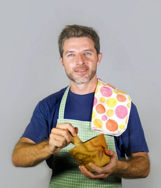 young attractive and happy home cook man with apron and kitchen cloth grinding ingredient using mortar smiling satisfied and cheerful in domestic successful cooking and househusband concept