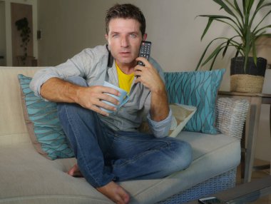 Genç yakışıklı ve konsantre adam televizyon izlerken ev ya da ilginç ve hayret seyir Haberler, oturma odası kanepe koltuk eğlence ve yaşam tarzı kavramı içinde oturan