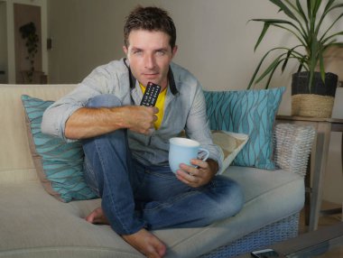 Evde televizyon film veya oturma odası kanepe oturma zevk programı holding uzaktan kumanda yaşam tarzı kavramında kanepe izlerken genç çekici mutlu ve yakışıklı adam rahat