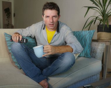 genç çekici şaşırttı ve rahat kıyafetler evde erkekte uyuşukluk ifade güvensizlik ve tv haber ya da uzaktan kumanda tutan oturma odası koltuk kanepe üzerinde film izlerken sürpriz ile şok 