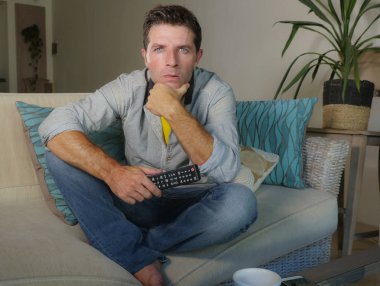 Genç yakışıklı ve konsantre adam televizyon izlerken ev ya da ilginç ve hayret seyir Haberler, oturma odası kanepe koltuk eğlence ve yaşam tarzı kavramı içinde oturan