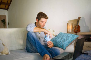 çevirmen ve bağımsız iş iş kavramı mutlu kahve içme dizüstü bilgisayarda ağ kanepede oturan ev oturma odasından çalışan genç çekici ve başarılı erkeğin