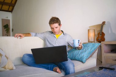 çevirmen ve bağımsız iş iş kavramı mutlu kahve içme dizüstü bilgisayarda ağ kanepede oturan ev oturma odasından çalışan genç çekici ve başarılı erkeğin