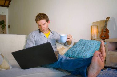 çevirmen ve bağımsız iş iş kavramı mutlu kahve içme dizüstü bilgisayarda ağ kanepede oturan ev oturma odasından çalışan genç çekici ve başarılı erkeğin