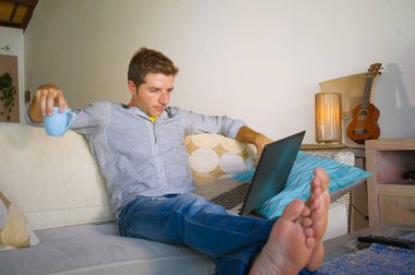 çevirmen ve bağımsız iş iş kavramı mutlu kahve içme dizüstü bilgisayarda ağ kanepede oturan ev oturma odasından çalışan genç çekici ve başarılı erkeğin