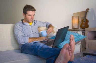 çevirmen ve bağımsız iş iş kavramı mutlu kahve içme dizüstü bilgisayarda ağ kanepede oturan ev oturma odasından çalışan genç çekici ve başarılı erkeğin