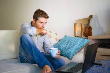 çevirmen ve bağımsız iş iş kavramı mutlu kahve içme dizüstü bilgisayarda ağ kanepede oturan ev oturma odasından çalışan genç çekici ve başarılı erkeğin