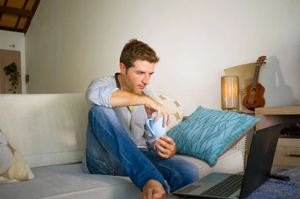çevirmen ve bağımsız iş iş kavramı mutlu kahve içme dizüstü bilgisayarda ağ kanepede oturan ev oturma odasından çalışan genç çekici ve başarılı erkeğin