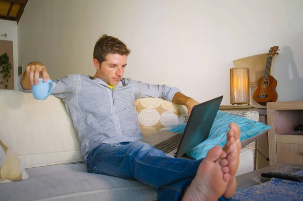 çevirmen ve bağımsız iş iş kavramı mutlu kahve içme dizüstü bilgisayarda ağ kanepede oturan ev oturma odasından çalışan genç çekici ve başarılı erkeğin