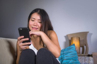 cep telefonu gülümseyen üzerinde Internet Sosyal medya app eğlence evde kanepe koltuk online iletişim yaşam tarzı kavramı içinde neşeli kullanan genç tatlı mutlu ve pretty Asya Kore kadın