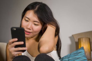 cep telefonu gülümseyen üzerinde Internet Sosyal medya app eğlence evde kanepe koltuk online iletişim yaşam tarzı kavramı içinde neşeli kullanan genç tatlı mutlu ve pretty Asya Kore kadın