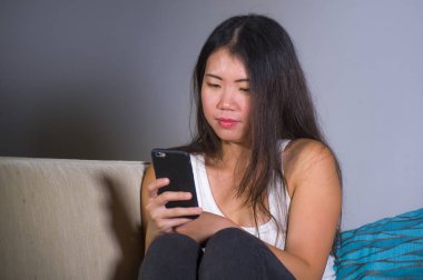 Genç tatlı mutlu ve güzel Asya internet sosyal medya app kullanarak cep telefonu gülümseyen kadın evde kanepe koltuk online iletişim yaşam tarzı kavramı içinde oturan rahat Korece