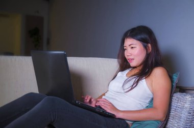 Genç güzel Asyalı Koreli öğrenci kız mutlu ve evde rahat koltuk kanepe üzerinde dizüstü bilgisayar ağ online teknoloji iletişim yaşam tarzı kavramı içinde neşeli internet kullanımı 