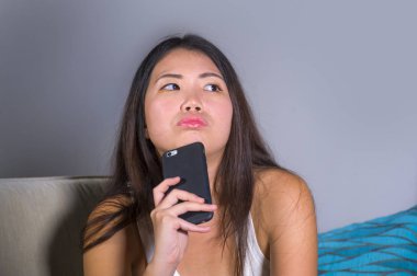 evde kanepe çevrimiçi iletişim yaşam tarzı içinde oturan dalgın ve düşünceli arıyorum cep telefonunda internet sosyal medya app kullanarak genç tatlı mutlu ve güzel Asyalı Koreli kız