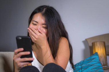 İnternet sosyal medya app cep telefonu evde kanepe koltuk çevrimiçi iletişim yaşam tarzı kavram eğleniyor neşeli gülüyor kullanan genç tatlı mutlu ve pretty Asya Kore kadın