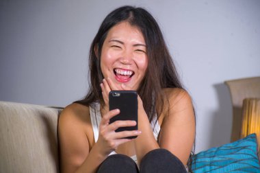 İnternet sosyal medya app cep telefonu evde kanepe koltuk çevrimiçi iletişim yaşam tarzı kavram eğleniyor neşeli gülüyor kullanan genç tatlı mutlu ve pretty Asya Çinli kız