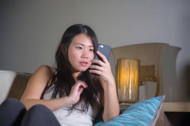 cep telefonu gülümseyen üzerinde Internet Sosyal medya app eğlence evde kanepe koltuk online iletişim yaşam tarzı kavramı içinde neşeli kullanan genç tatlı mutlu ve pretty Asya Kore kadın
