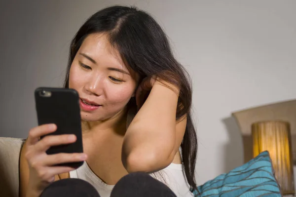 年轻甜美快乐和漂亮的亚洲韩国妇女使用互联网社交媒体应用程序在手机上微笑愉快地在家沙发沙发上的乐趣在线交流生活方式概念 — 图库照片