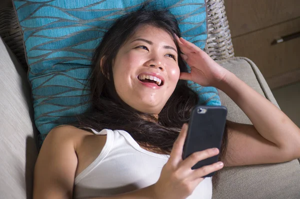 İnternet sosyal medya app üstünde hareket eden telefon ev kanepe koltuk online iletişim yaşam tarzı kavramı içinde neşeli yatan gülümseyen kullanan genç tatlı mutlu ve pretty Asya Çinli kız