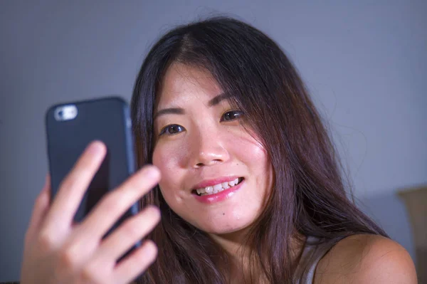 young sweet happy and pretty Asian Korean girl taking selfie picture with mobile phone for internet social media on mobile phone laughing at home in online communication lifestyle concept
