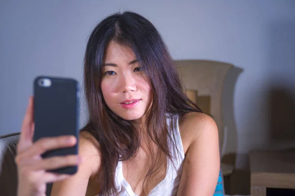 young sweet happy and pretty Asian Korean woman taking selfie picture with mobile phone for internet social media on mobile phone laughing at home in online communication lifestyle concept