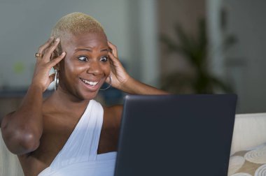 evde dizüstü bilgisayar üzerinde çalışan gülümseyen genç güzel mutlu siyah afro Amerikalı kadın girişimci bağımsız çalışma ve Internet serbest iş kanepe kanepede rahat