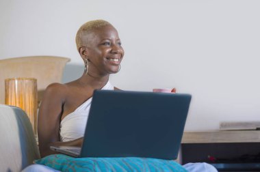 evde dizüstü bilgisayar üzerinde çalışan gülümseyen genç güzel mutlu siyah afro Amerikalı kadın girişimci bağımsız çalışma ve Internet serbest iş kanepe kanepede rahat